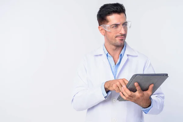 Fiatal jóképű férfi orvos védőszemüveg gondolkodás használata közben a digitális tabletta — Stock Fotó