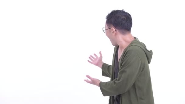 Счастливый японский мужчина в очках, показывающий на спину и выглядящий взволнованным — стоковое видео