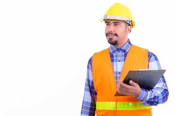 Feliz barbudo hombre persa trabajador de la construcción pensando mientras sostiene portapapeles —  Fotos de Stock