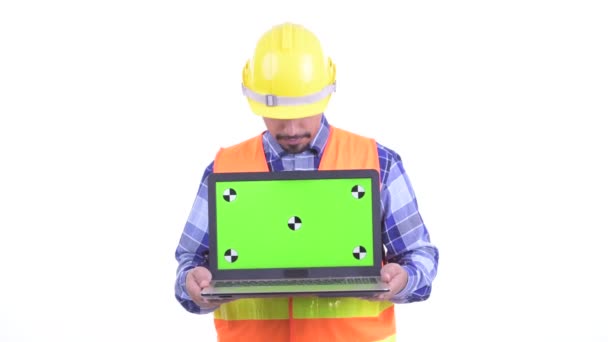 Happy bearded Persian man construction worker thinking while showing laptop — Stock Video