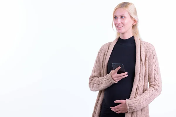 Gelukkige jonge blonde zwangere vrouw denken tijdens het gebruik van de telefoon — Stockfoto