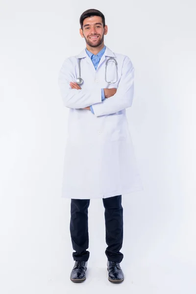 Cuerpo completo de feliz joven barbudo médico hombre persa sonriendo con los brazos cruzados —  Fotos de Stock