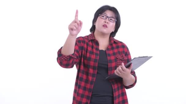 クリップボードを保持しながら指を指す幸せな太りすぎアジアのヒップ女性 — ストック動画