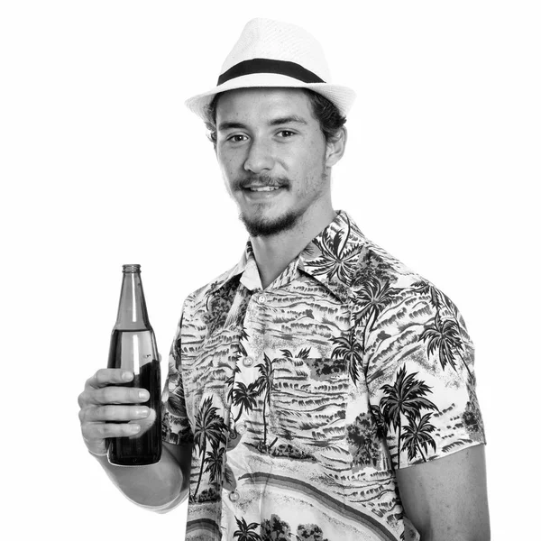 Студийный снимок молодого счастливого туриста, улыбающегося, держа бутылку пива на белом фоне — стоковое фото