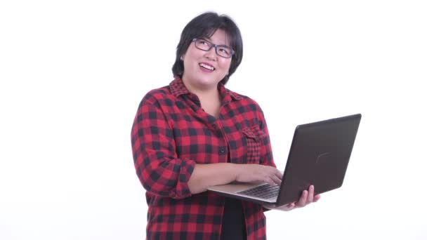 Happy overweight Asian hipster woman thinking while using laptop — Stock Video