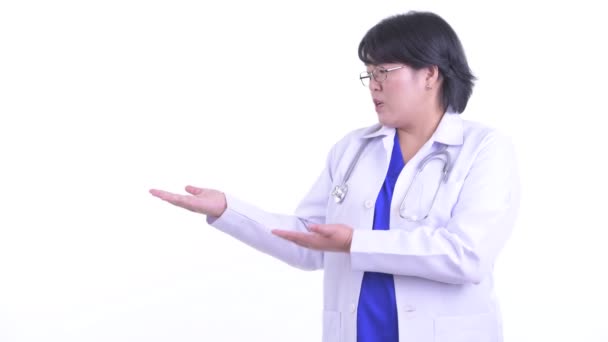 Stressed overweight Asian woman doctor talking while showing something — Stock Video