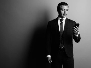 Gri arka plana karşı cep telefonu kullanırken takım elbise giyen işadamı