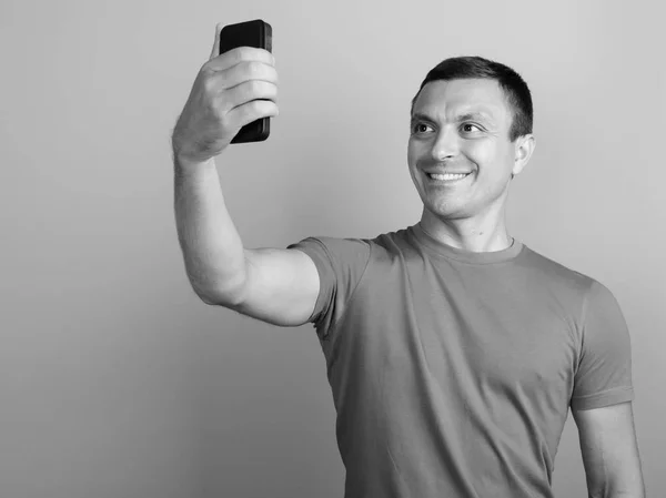Мужчина в футболке во время использования мобильного телефона на сером фоне — стоковое фото
