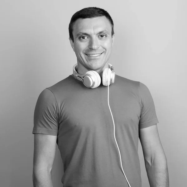 Człowiek ubrany w t-shirt i słuchawki wokół szyi na szarym tle — Zdjęcie stockowe