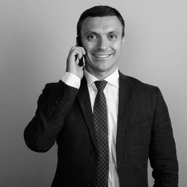 Empresario que usa traje mientras usa el teléfono móvil contra fondo gris —  Fotos de Stock