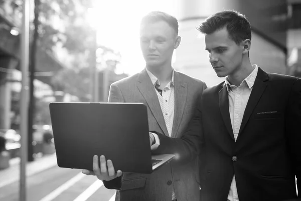 Twee zakenlieden die buiten samenwerken met een laptop computer — Stockfoto