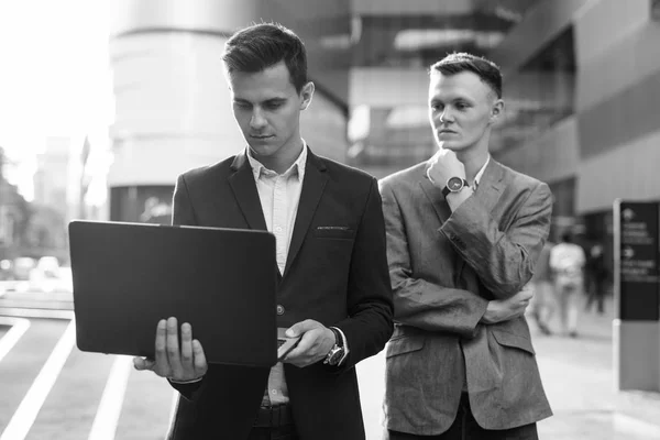 Twee zakenlieden die buiten samenwerken met een laptop computer — Stockfoto