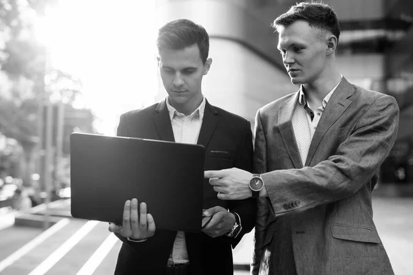Twee zakenlieden die buiten samenwerken met een laptop computer — Stockfoto