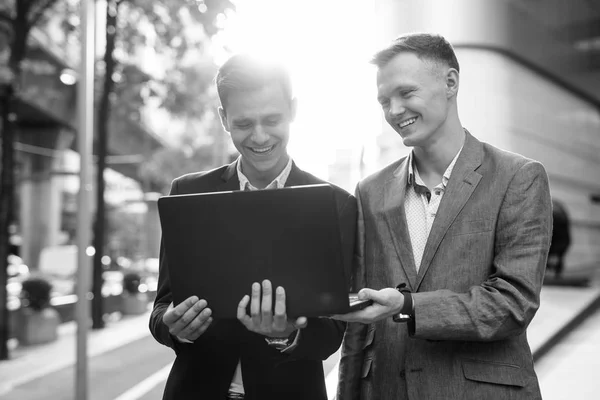 Twee zakenlieden die buiten samenwerken met een laptop computer — Stockfoto