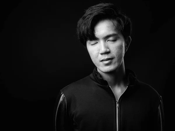 Young handsome Asian man against black background — Stock Photo, Image