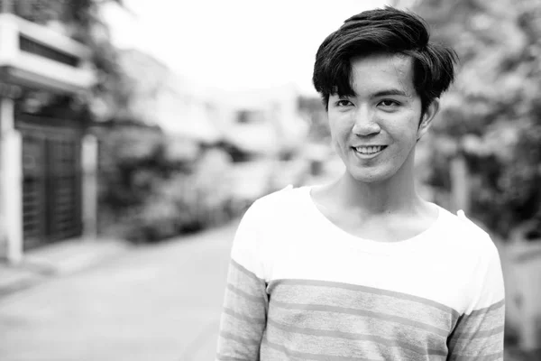 Joven guapo asiático hombre sonriendo y pensando al aire libre —  Fotos de Stock