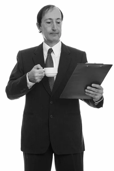 Studio shot van volwassen zakenman met koffiekop tijdens het lezen op klembord — Stockfoto