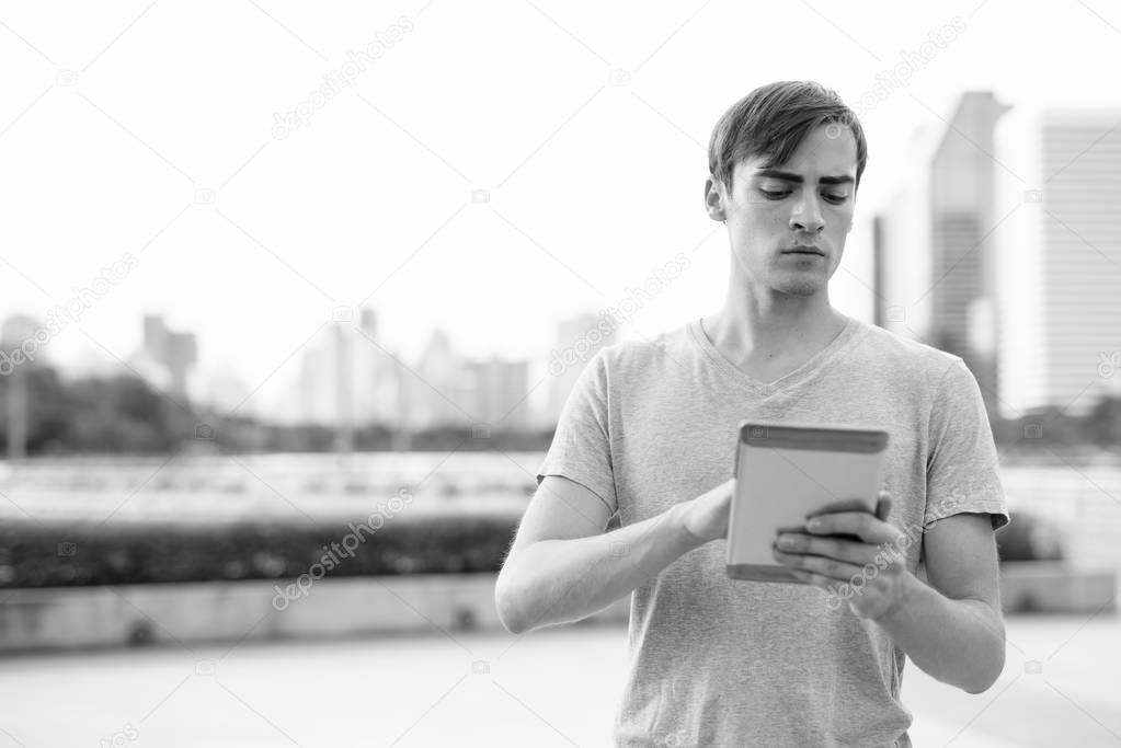 Young handsome man using digital tablet while relaxing at the park
