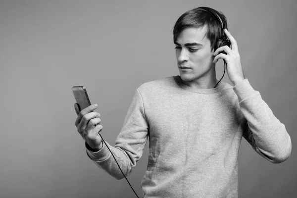 Junger, gutaussehender Mann hört Musik und ist bereit für das Fitnessstudio vor grauem Hintergrund — Stockfoto