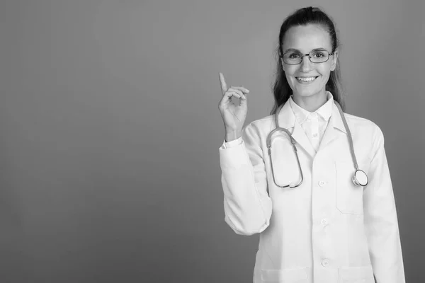 Jovem mulher bonita médico mostrando espaço cópia contra fundo cinza — Fotografia de Stock