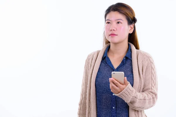 Joven mujer asiática pensando mientras usa el teléfono listo para el invierno —  Fotos de Stock