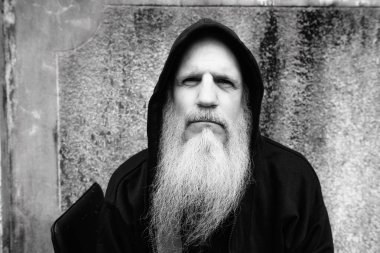 Portrait of mature bald man with long gray beard against grunge concrete wall outdoors in black and white