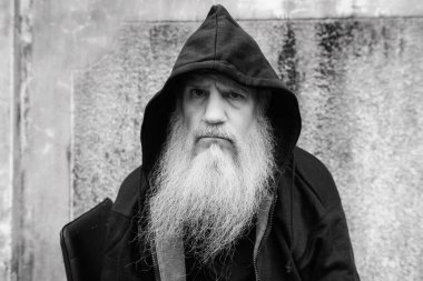 Portrait of mature bald man with long gray beard against grunge concrete wall outdoors in black and white