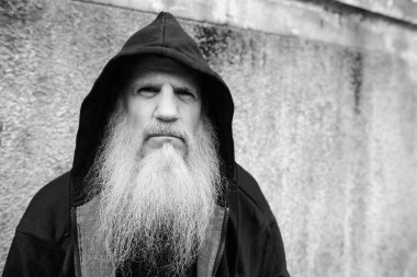 Portrait of mature bald man with long gray beard against grunge concrete wall outdoors in black and white
