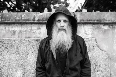 Portrait of mature bald man with long gray beard against grunge concrete wall outdoors in black and white