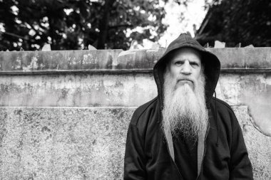 Portrait of mature bald man with long gray beard against grunge concrete wall outdoors in black and white