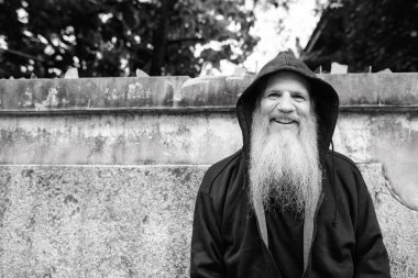 Portrait of mature bald man with long gray beard against grunge concrete wall outdoors in black and white