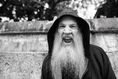 Portrait of mature bald man with long gray beard against grunge concrete wall outdoors in black and white