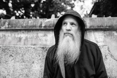 Portrait of mature bald man with long gray beard against grunge concrete wall outdoors in black and white