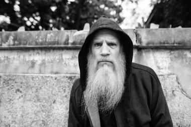 Portrait of mature bald man with long gray beard against grunge concrete wall outdoors in black and white