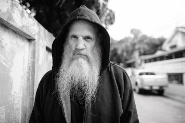 Portrait of mature bald man with long gray beard against grunge concrete wall outdoors in black and white