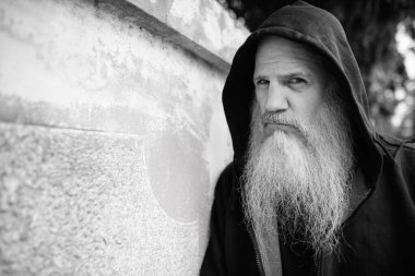 Portrait of mature bald man with long gray beard against grunge concrete wall outdoors in black and white