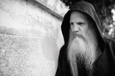 Portrait of mature bald man with long gray beard against grunge concrete wall outdoors in black and white