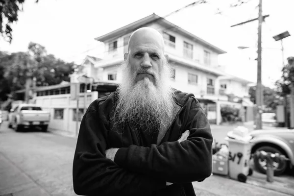 Portrait of mature bald man with long gray beard in the streets outdoors in black and white