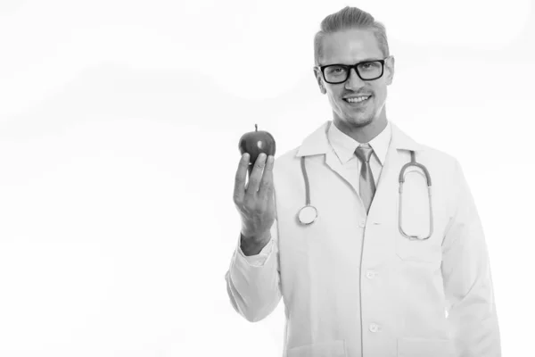 Στούντιο πλάνο του ευτυχισμένος νεαρός όμορφος γιατρός χαμογελά κρατώντας κόκκινο μήλο — Φωτογραφία Αρχείου