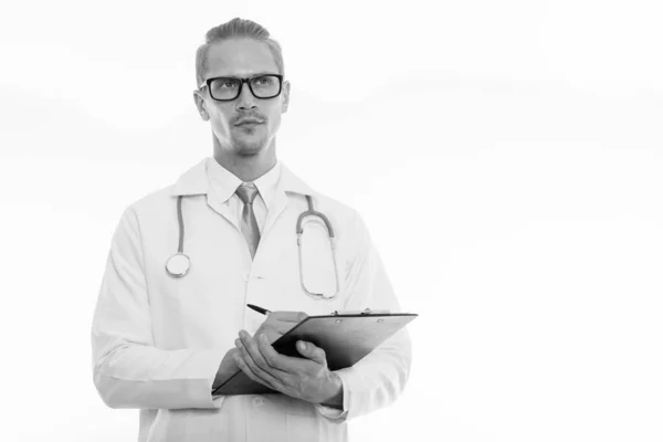 Estudio de la toma de joven guapo médico hombre escribiendo en el portapapeles, mientras que pensar y mirar hacia arriba —  Fotos de Stock