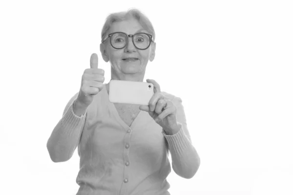 Heureuse femme nerd âgée souriante tout en prenant des photos avec téléphone mobile et en donnant pouce vers le haut — Photo