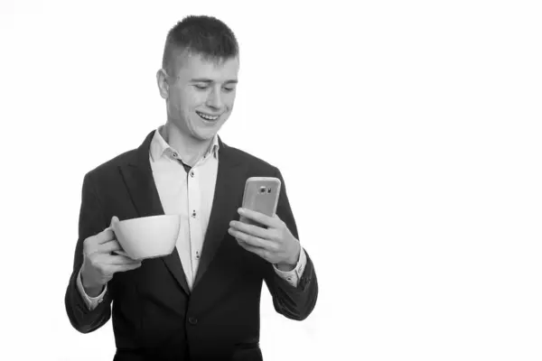 Studio colpo di giovane uomo d'affari felice sorridente e in possesso di tazza di caffè durante l'utilizzo del telefono cellulare — Foto Stock