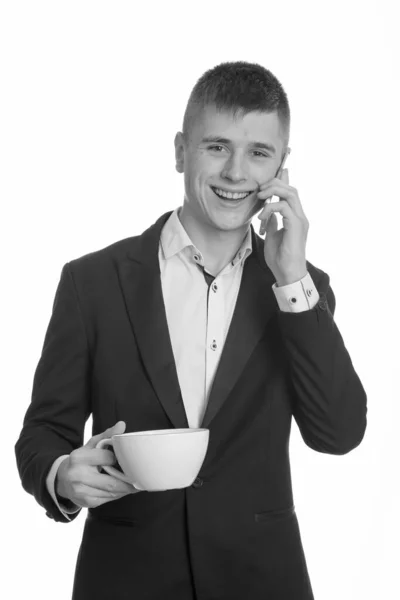 스튜디오에서 젊고 행복 한 사업가가 휴대폰으로 이야기하면서 웃고 커피 잔을 들고 있는 모습 — 스톡 사진