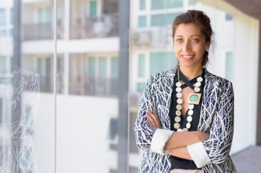 Ofis binasının penceresinden kollarını kavuşturup gülümseyen mutlu İspanyol iş kadını.