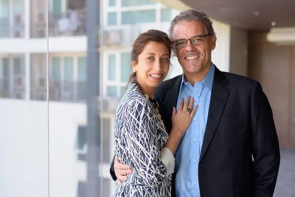 Feliz pareja de negocios hispanos sonriendo juntos por la ventana del edificio de oficinas — Foto de Stock