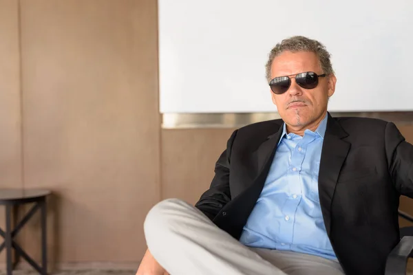 Hombre de negocios hispano maduro con gafas de sol sentado en la oficina — Foto de Stock