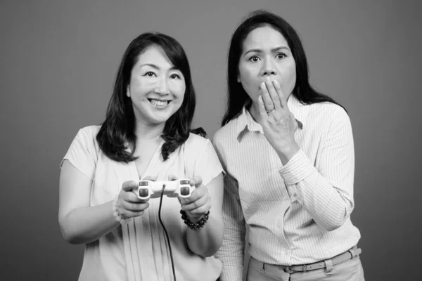 Duas mulheres de negócios asiáticas maduras jogando jogos de vídeo juntas — Fotografia de Stock