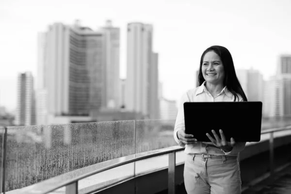 Зрелая азиатская бизнесвумен, использующая ноутбук в городе — стоковое фото