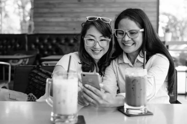 Дві зрілі азіатські жінки разом тусуються у кав "ярні, розважаючись. — стокове фото