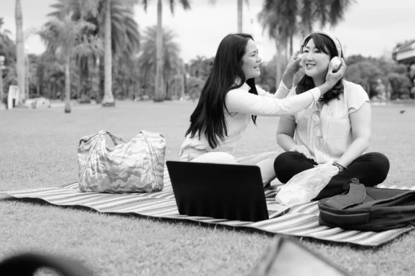 아시아 여성 두 명 이 공원에서 휴식을 취하고 노트북 컴퓨터를 사용하는 모습 — 스톡 사진